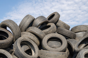 a lot of used tyres against blue sky with white clouds.
