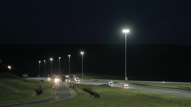 Cars and trucks on the highway. Suburban car traffic on the road at night. Turn around and go straight. Dark city in the background. Night lighting. Lanterns at night along the road. Dark background.