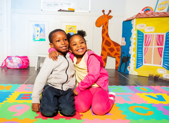 Two siblings boy, girl in play room hug and smile