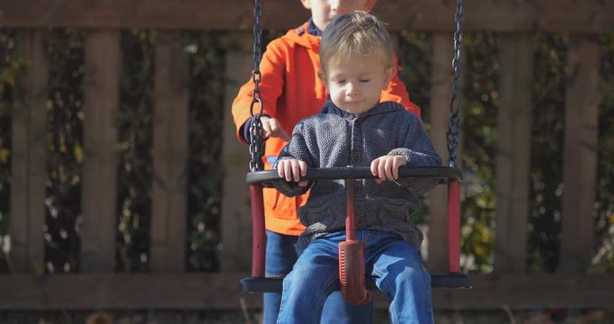Big brother pushing baby swing in park, strong relationship