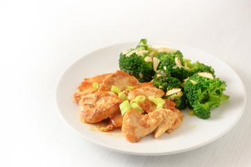 marinated chicken breast fillet with spring onions and broccoli with almond sticks as a healthy meal with little carbohydrates for slimming on a plate, background is blending to white, copy space