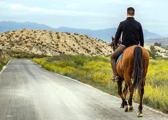 A young rider riding his horse on a mountain road