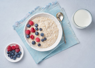 Oatmeal with blueberries, raspberries and cup of milk on blue light background. Top view. Healthy diet breakfast