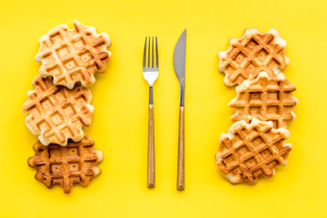 Homemade Viennese waffles and fork with knife on yellow background top view