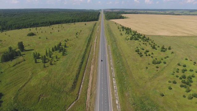 Flying over the straight road. The movement of cars on the road. Top view on the car, forest, field. Summer video from the drone. Rural landscape.