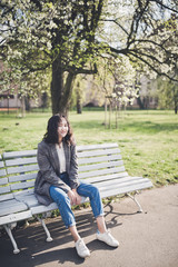 Cheerful asian young woman sitting on a bench under the blooming trees in a park