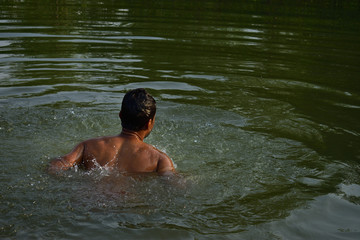 A man bathing in a natural lake, refreshing himself from heat of summer in summer season in rural India, at Nature Reserve.