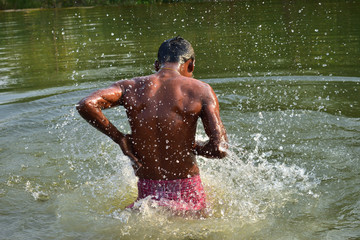 A man bathing in a natural lake, refreshing himself from heat of summer in summer season in rural India, at Nature Reserve.