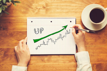Market up trend chart with a person holding a pen on a wooden desk