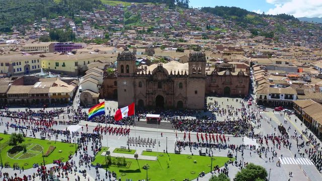 Aerial view of Cusco's main plaza with parade and crowd of people watching the national flag raising act. Marching band, Peruvian and Tahuantinsuyo flag weaving at the Sunday ceremony.