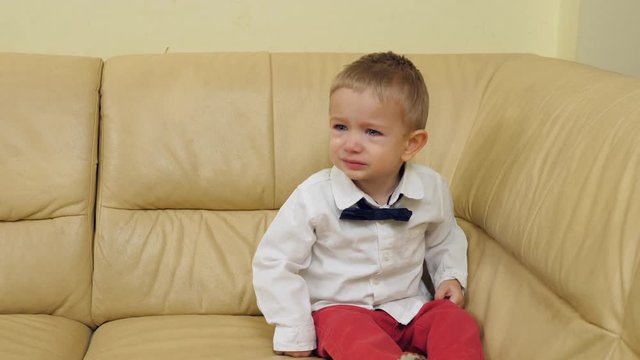 Elegant baby child sitting on sofa and crying, lonely kid with bow