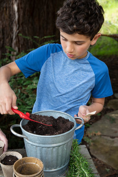 Boy scooping soil into pots to plant seeds in the garden