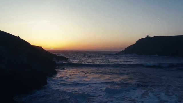 Drone captures a setting sun at golden hour over a lonely cove. Haze and setting sun create a dreamy and surreal vibe.