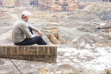 A man sits and looks from a height at the ruins of a zinc plant, destroyed brick buildings, the remains of the walls. The view from the back.