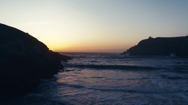 Drone captures a setting sun at golden hour over a lonely cove. Haze and setting sun create a dreamy and surreal vibe.