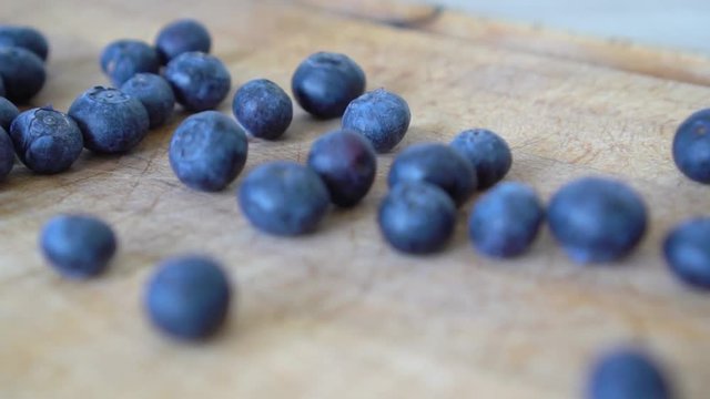 Close up slow motion shot of blueberries rolling on a wooden cutting board, thrown by a man on the left side