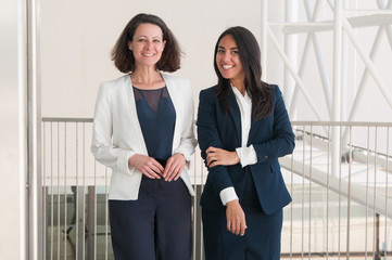 Two happy business women posing at camera in office hall