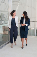 Two smiling female colleagues walking in office hall