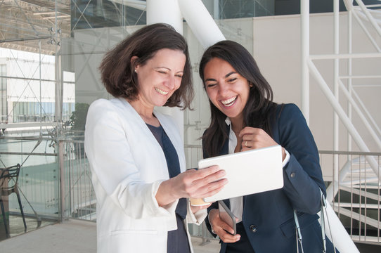 Two smiling business women using tablet in office hall