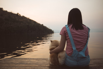 Woman sit and relax with her dog admire the sunset sky and the lake.