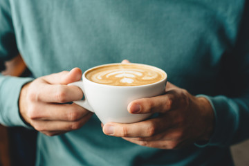 A man in a blue jumper holding a cup of cappuccino in his hands during breakfast