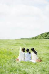 草原でピクニックをする3人の女性の後姿