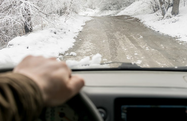 Man's hand on the steering wheel of a car that moves in the snowy forest on a wet slushy road