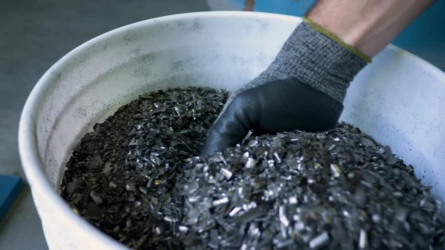 Gloved hand picks up metal flakes at metal recycling plant