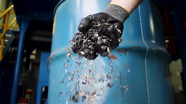 Gloved hand drops metal turnings into a bucket