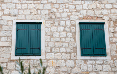 the stone wall of the house is light with shuttered windows