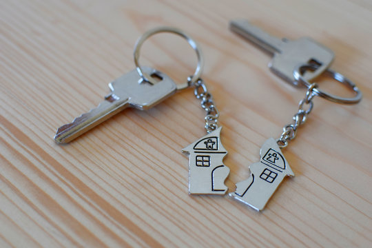Pendant of key ring in shape of house divided in two parts on wooden background, closeup view. Dividing house when divorce, division of property and real estate.