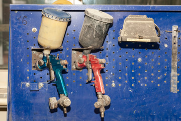 Two body paint gun sprayer red and blue installed on a workbench in a vehicle repair workshop next to another tool and lamp. Industry in auto service