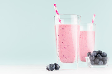 Purple milk cocktails with blueberries in bowl, striped straws in elegant glass in soft light mint green interior,  copy space.