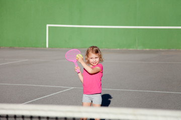 Fototapeta na wymiar Kid is playing tennis on court. Cute child is having fun playing sports activities outdoors. Little girl has practice in summer game.