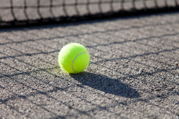 One tennis ball by net on tennis court. Concept of workout, summer sports activities and playing outdoors.
