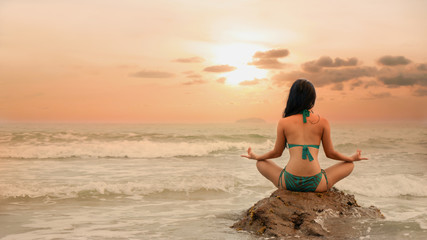 Fototapeta na wymiar natural background of Asian female in bikini having yoga and meditation on the rock in sea near beach during sunset