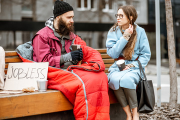 Homeless beggar with young woman listening to his sad story while sitting together on the bench...
