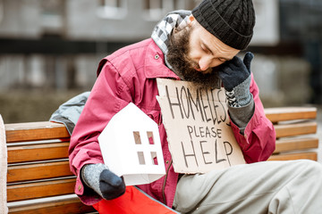 Homeless beggar holding paper house and message for help on a cardboard begging and grieving for a...