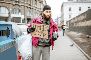 Portrait of a depressed homeless beggar with cardboard begging some money on the street in the city