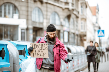 Portrait of a depressed homeless beggar with cardboard begging some money on the street in the city