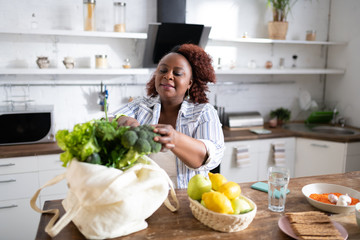 Cheerful curly haired woman taking broccoli from bag