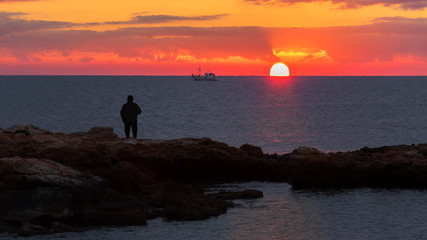 Fototapeta premium An angler fishes in the Mediterranean on the rocky coast at Torrevieja in the morning at sunrise