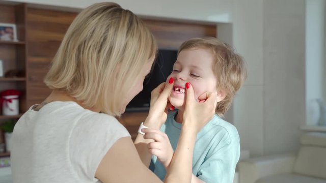 Mothers hand lovingly holding chin of small smiling handsome boy showing his white funny child teeth at home. Happy family relations, healthcare and dental problems concept