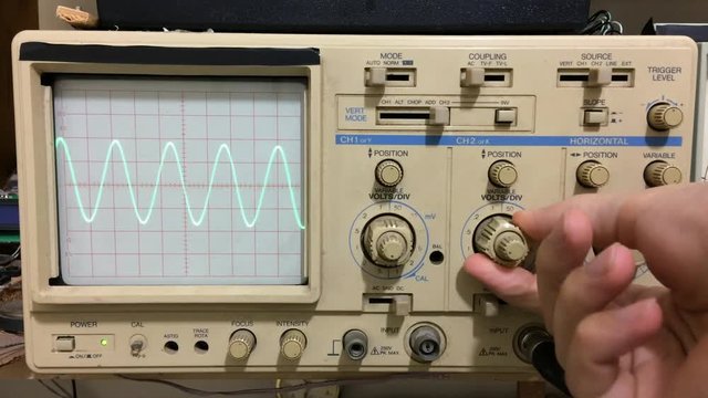 Electronics working with oscilloscope and sine wave shown on oscilloscope