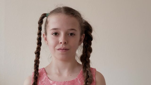 Junges M&auml;dchen mit Zahnspange und Z&ouml;pfen schaut ernst  in die Kamera , dann l&auml;chelt