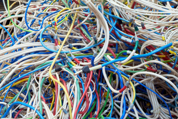 Many confusing between an electrical wires of different colors. Chaos, confusion, disorder. Wires or cables are white, red, blue, yellow, green. The bundle of wires is impossible to untangle.