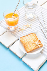 Breakfast toast, orange juice, water for children in the marine theme, creative with shells on a blue background