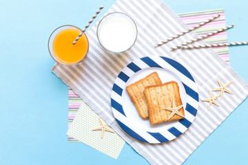 Breakfast toast, orange juice, water for children in the marine theme, creative with shells on a blue background