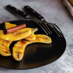 Fried bananas with syrup on the black plate. Cinnamon dusted plantains pan fried in butter is a popular dessert in Mexico and other South Latin American countries.