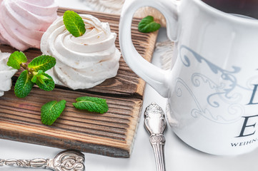 White creamy marshmallow handmade. Adorned with mint leaves. Tea in a white cup with a blue ornament. On a wooden background. Close-up.